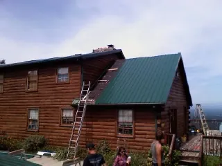 Green metal roof going on a two story log home with ladders set in Murfreesboro